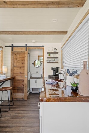Una cocina con puerta de madera, armarios blancos y encimera con varios objetos.