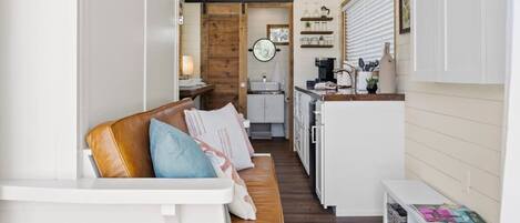 A compact, open-plan living space with a wooden bench, a kitchen area, and a dining table.