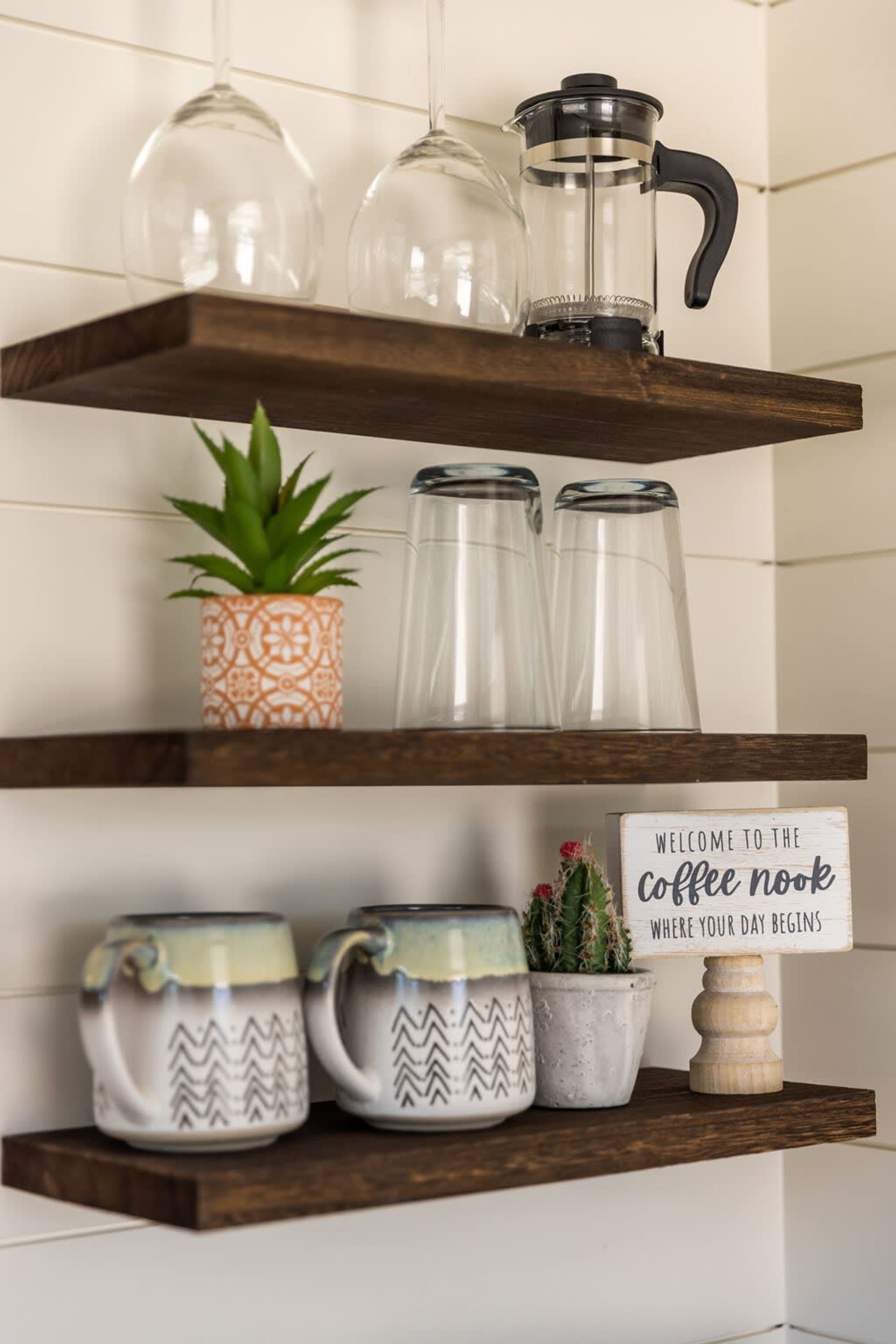A kitchen shelf with glassware, a coffee maker, and a sign that reads "Welcome to the coffee nook where your day begins."