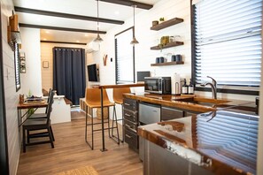 A modern kitchen with wooden countertops, a built-in microwave, and a stainless steel sink. There are two bar stools and a dining table with chairs.