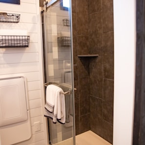 A bathroom with a glass shower enclosure, a towel rack with a towel, and two wall-mounted baskets.