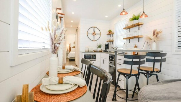 A modern kitchen with white cabinetry, a central island, bar stools, and pendant lighting. - New Luxury Shipping Container (Waco)