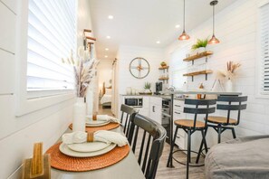 A modern kitchen with white cabinetry, a central island, bar stools, and pendant lighting. - New Luxury Shipping Container (Waco)
