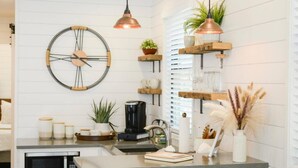 A modern kitchen with a large wall clock, pendant lights, wooden shelves, and various kitchen appliances. - New Luxury Shipping Container (Waco)