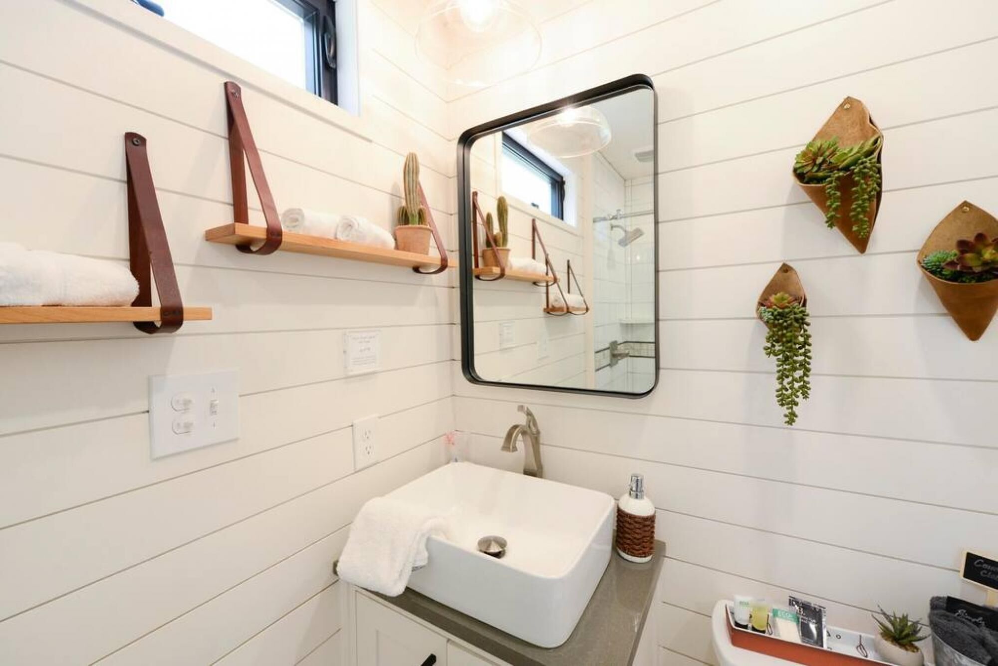 A modern bathroom with a white sink, a mirror, and wooden shelves with towels.