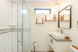 A modern bathroom with a glass shower enclosure, a white sink with a wooden countertop, and a mirror above the sink. - New Luxury Shipping Container (Waco)