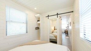 A bedroom with a bed, a walk-in closet, and a hallway leading to a bathroom. - New Luxury Shipping Container (Waco)