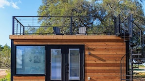 A modern cabin with a wooden exterior, large sliding glass doors, and a small balcony with solar panels. - New Wilderness Hideout-cozy Container Home (Fredericksburg)