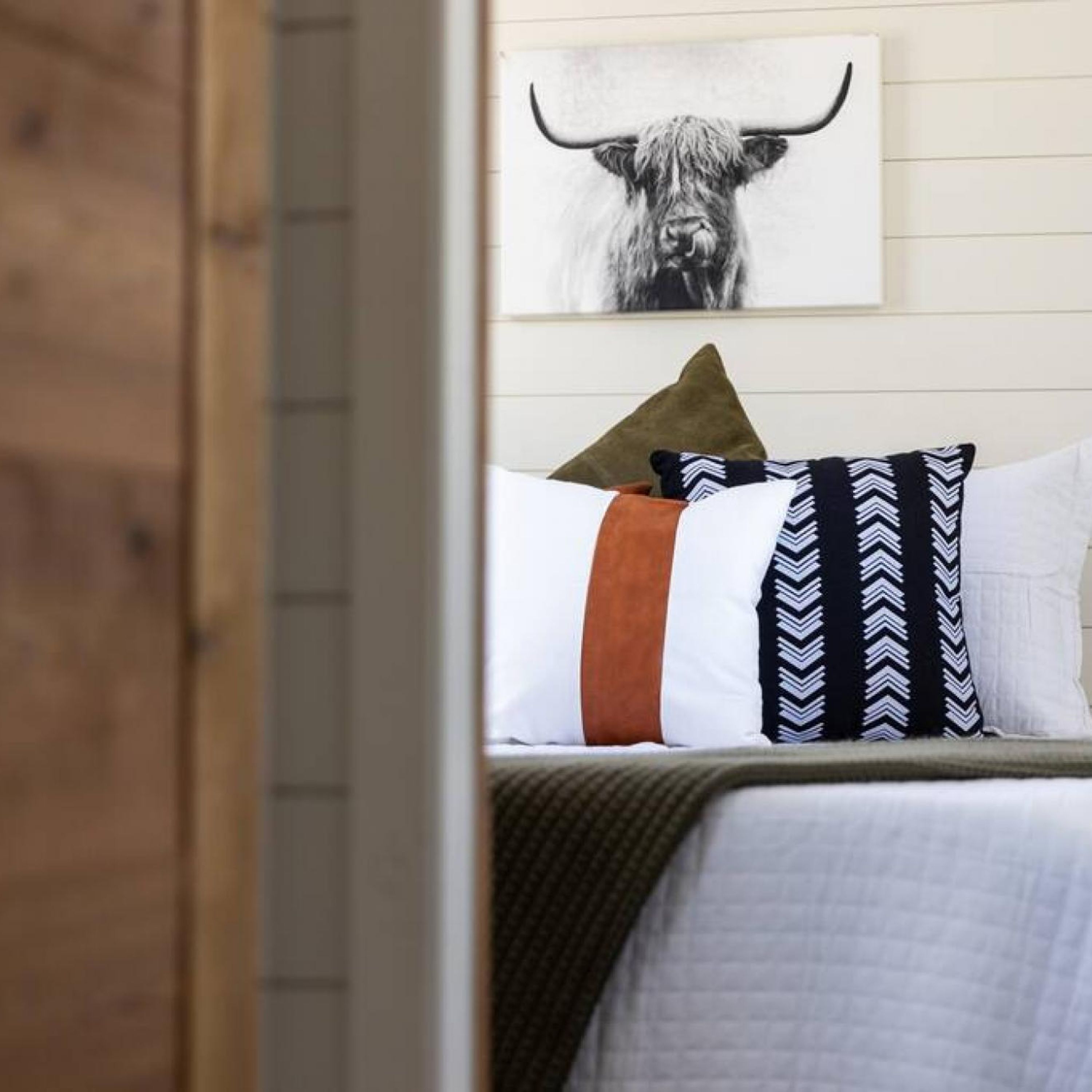 Une chambre à coucher avec un lit, des oreillers et une œuvre d’art représentant un taureau, accrochée au mur.
