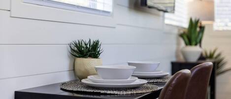 Un coin repas avec une table dressée pour deux personnes, comprenant une table noire, des assiettes blanches et un set de table en fibres tressées.