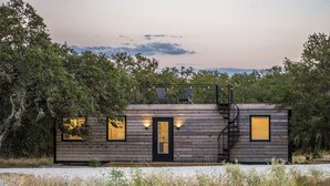 Een chalet met een houten gevel, een voordeur, een klein balkon met twee stoelen en een trap naar de bovenverdieping.