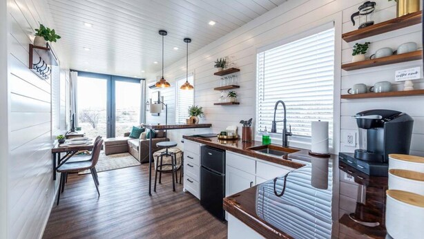 Una cocina moderna con armarios blancos, encimeras de madera, iluminación colgante y una estación de café integrada.