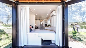 Une chambre compacte et moderne, dotée d’un lit, d’un petit bureau et d’une fenêtre donnant sur un jardin.