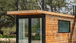 Une cabane en bois avec une porte et une fenêtre en verre, entourée d’arbres.