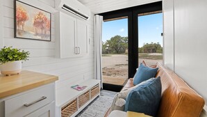 Un intérieur moderne avec un plafond en bois, des murs blancs, une grande fenêtre, un canapé avec des coussins, une plante et un tableau.