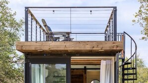 A compact, two-story cabin with a balcony and a spiral staircase. - New The Wildflower Cozy Container Home (Fredericksburg)