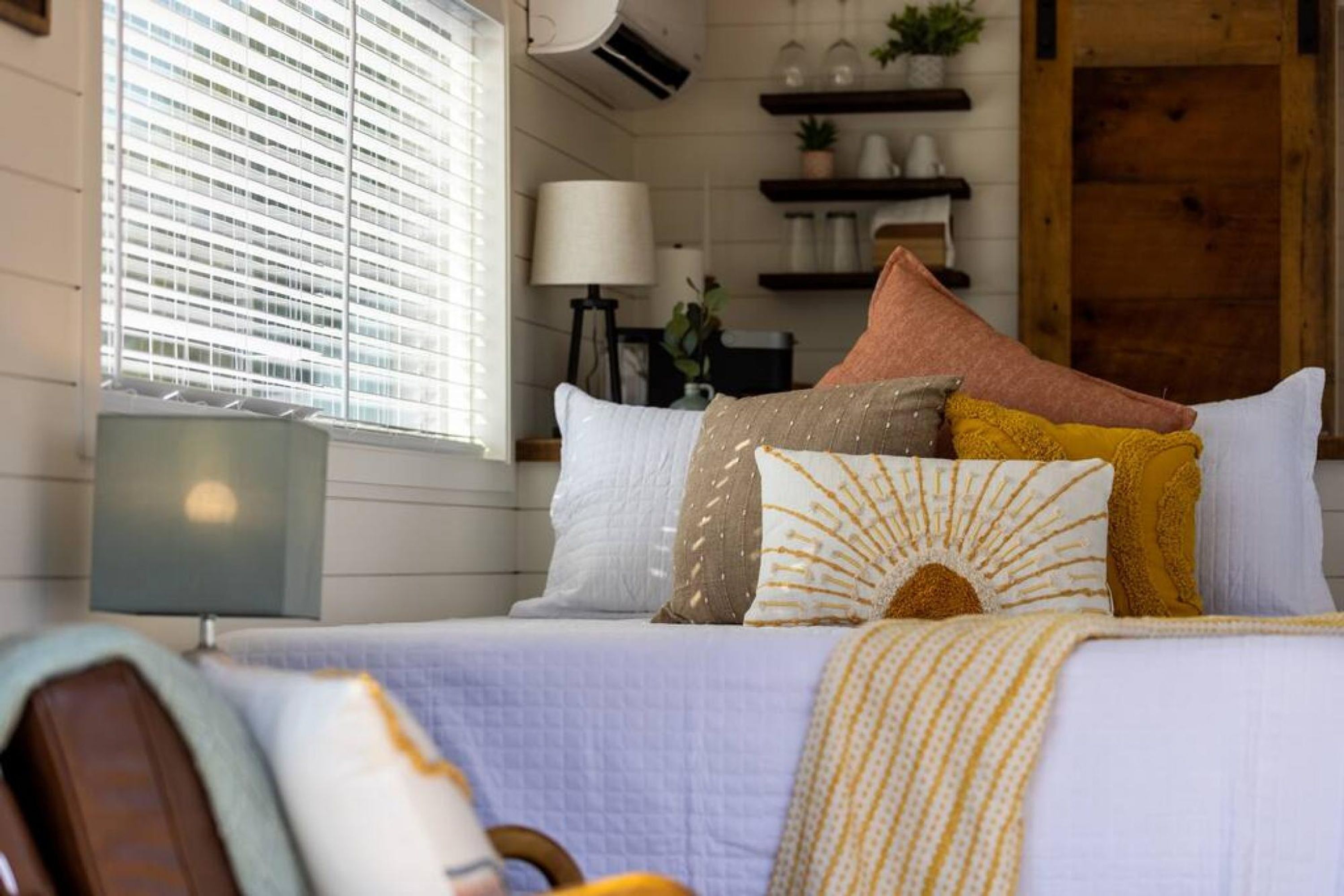 A neatly arranged bedroom with a bed, pillows, a lamp, and a window with blinds.