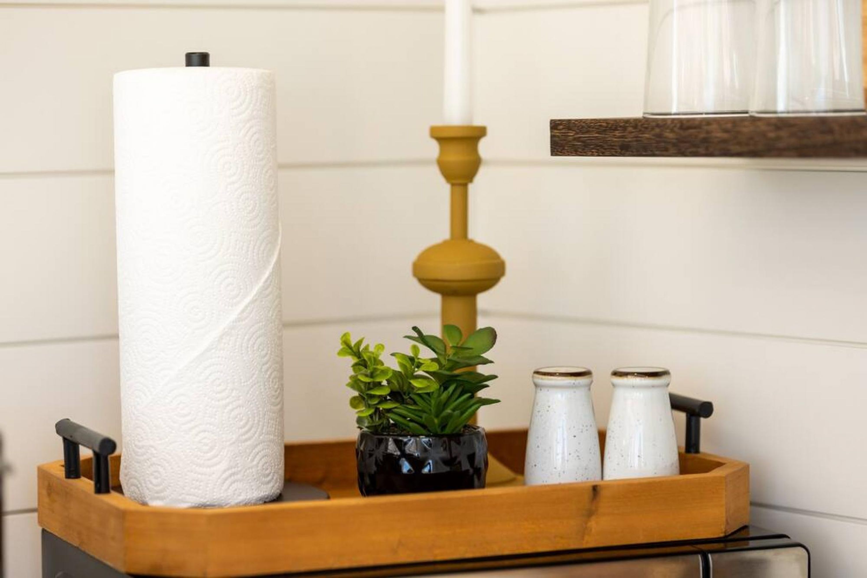 A bathroom with a toilet paper roll, a potted plant, and two salt and pepper shakers on a wooden tray.