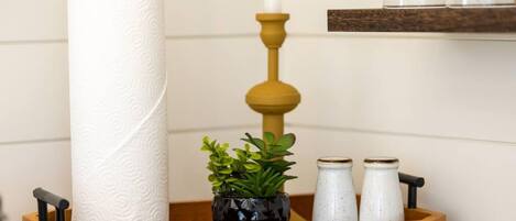 A bathroom with a toilet paper roll, a potted plant, and two salt and pepper shakers on a wooden tray.