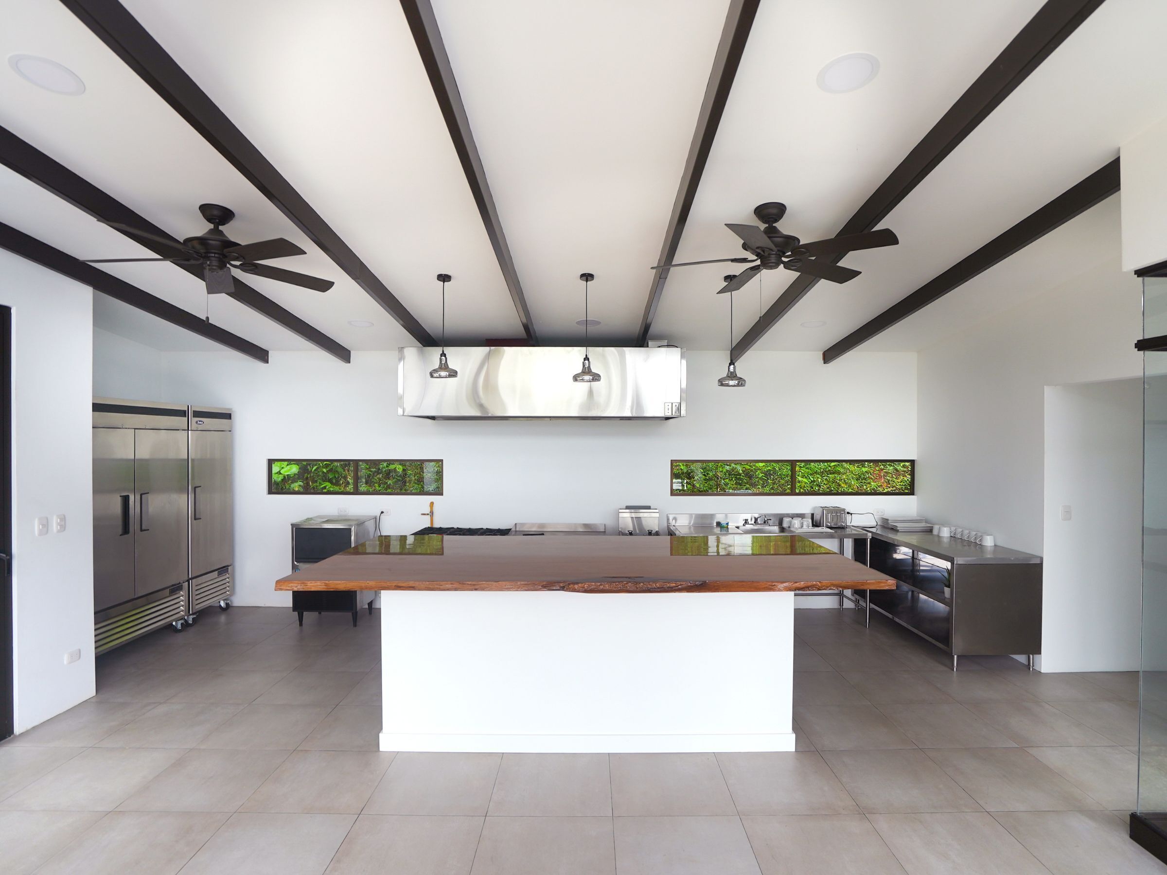 Een moderne keuken met een centraal eiland, plafondventilatoren, hanglampen en een roestvrijstalen koelkast.