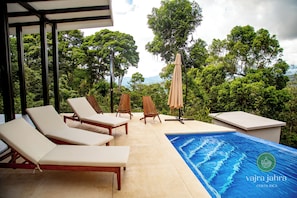 Un espace aménagé au bord de la piscine, avec des chaises longues, une piscine et une vue sur une végétation luxuriante.