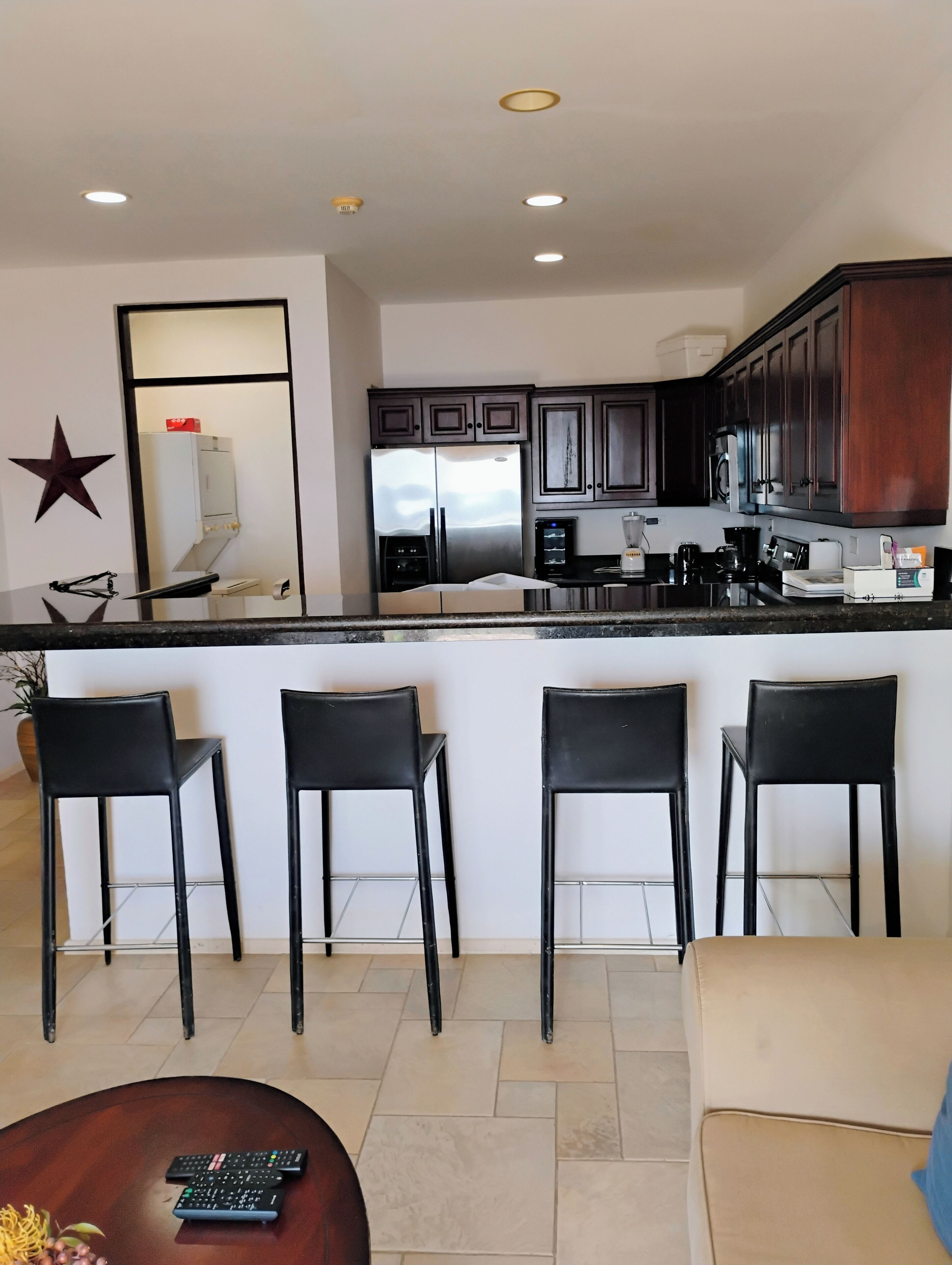 A modern kitchen with a central island, dark wooden cabinets, stainless steel appliances, and a bar area with four stools.