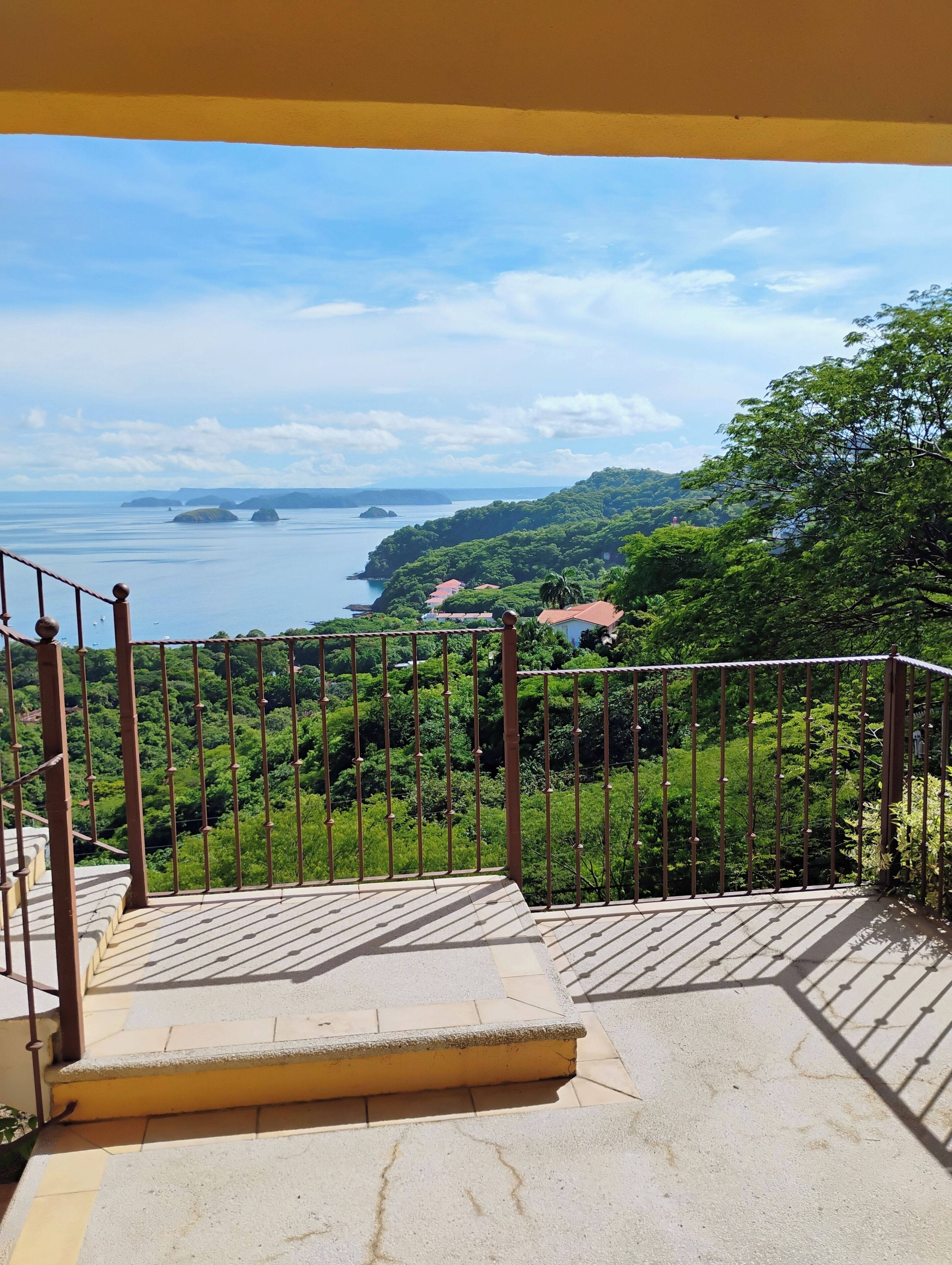 A balcony with a view of a coastal landscape, including a body of water and distant islands.
