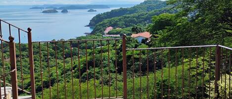 A balcony with a view of a coastal landscape, including a body of water and distant islands.