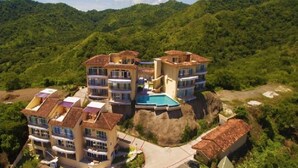 A multi-story hotel with a pool, surrounded by lush greenery and hills. - Extraordinary 2br Condo in Ocotal with amazing Bay and Ocean Views!  (Coco)