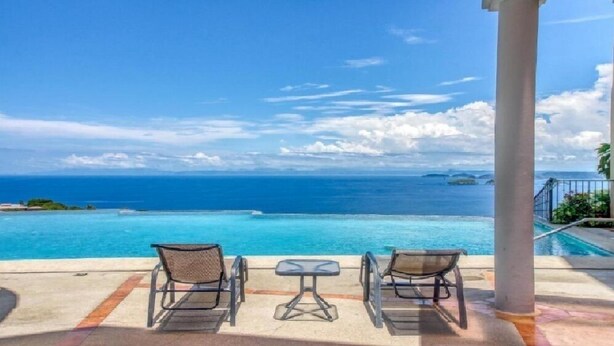 A poolside area with two chairs and a small table, overlooking a clear blue ocean with distant islands. - Extraordinary 2br Condo in Ocotal with amazing Bay and Ocean Views!  (Coco)