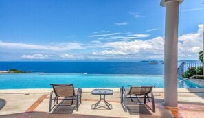 A poolside area with two chairs and a small table, overlooking a clear blue ocean with distant islands. - Extraordinary 2br Condo in Ocotal with amazing Bay and Ocean Views!  (Coco)