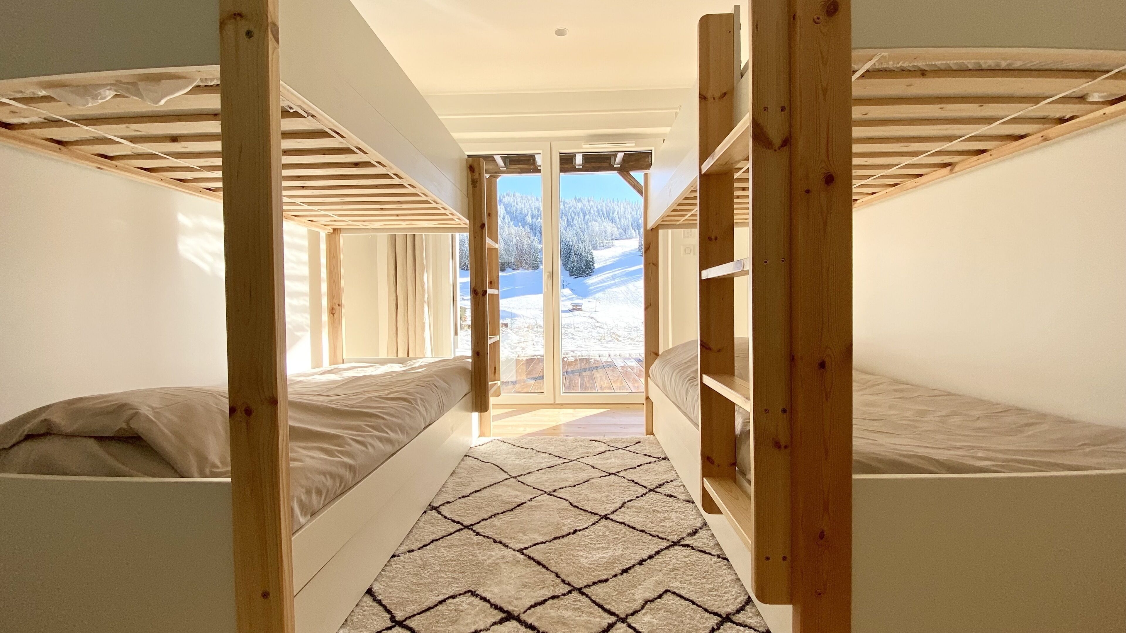 Ein Zimmer mit zwei Etagenbetten, einem großen Fenster und Blick auf eine verschneite Landschaft.