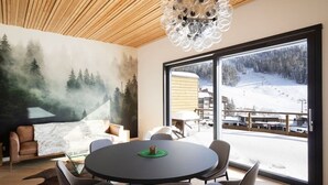Un interior moderno con una mesa redonda, sillas, un ventanal con vistas nevadas y un mural de un bosque en la pared.