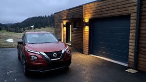 Un Nissan rojo estacionado frente a un edificio de madera con un garaje.