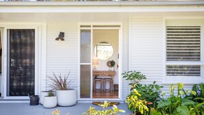 A white house with a front door, a small porch with potted plants, and a dining area visible through the open door.