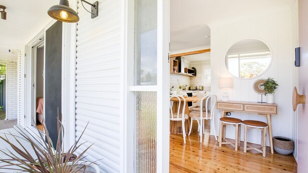 A modern kitchen with white cabinetry, a dining area with white chairs, and a large window providing natural light.