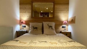 Une chambre avec un plafond en bois, deux tables de chevet avec des lampes, un lit avec une literie à motifs et un miroir au-dessus du lit.