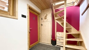 A wooden staircase with a red wall, a door with a red frame, and a black mat at the entrance. - Chalet Insolite, Cocooning, Poêle à Bois et ski (Prémanon)