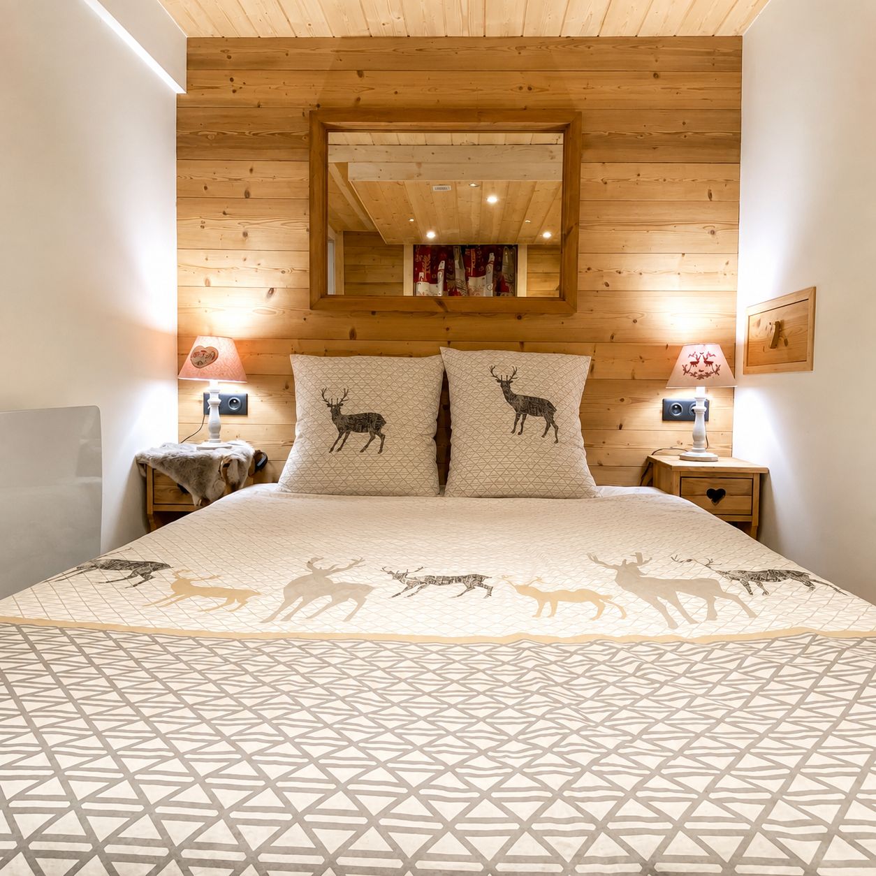 A bedroom with a wooden ceiling, two bedside tables with lamps, a bed with a patterned bedspread, and a mirror above the bed.