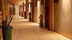 A wooden corridor with a high ceiling, wooden floors, and wall-mounted lighting fixtures. - Filho do Vento Kite Lodge (Canguaretama)