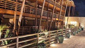 A wooden structure with a curved roof and multiple levels, surrounded by potted plants and a wooden deck. - Filho do Vento Kite Lodge (Canguaretama)
