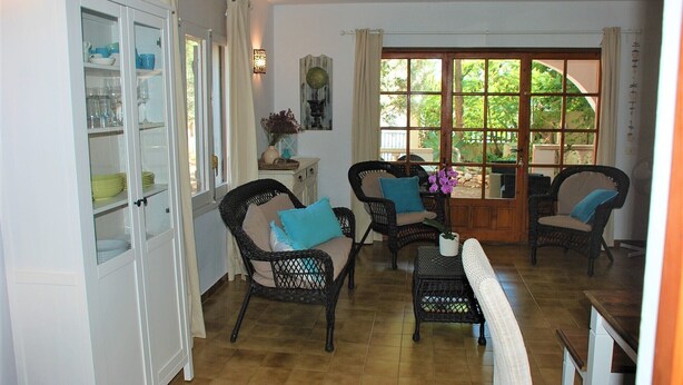 A spacious kitchen with a dining area, featuring wicker chairs, a cabinet with dishes, and a large window with a view of greenery. - SAONA VILLAS (VN MIANA): villa for 6 people, private swimming pool, air co (Les Tres Cales)