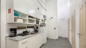Une cuisine moderne avec des meubles blancs, une machine à café, un four à micro-ondes et un évier. On peut voir une petite plante posée sur le plan de travail.