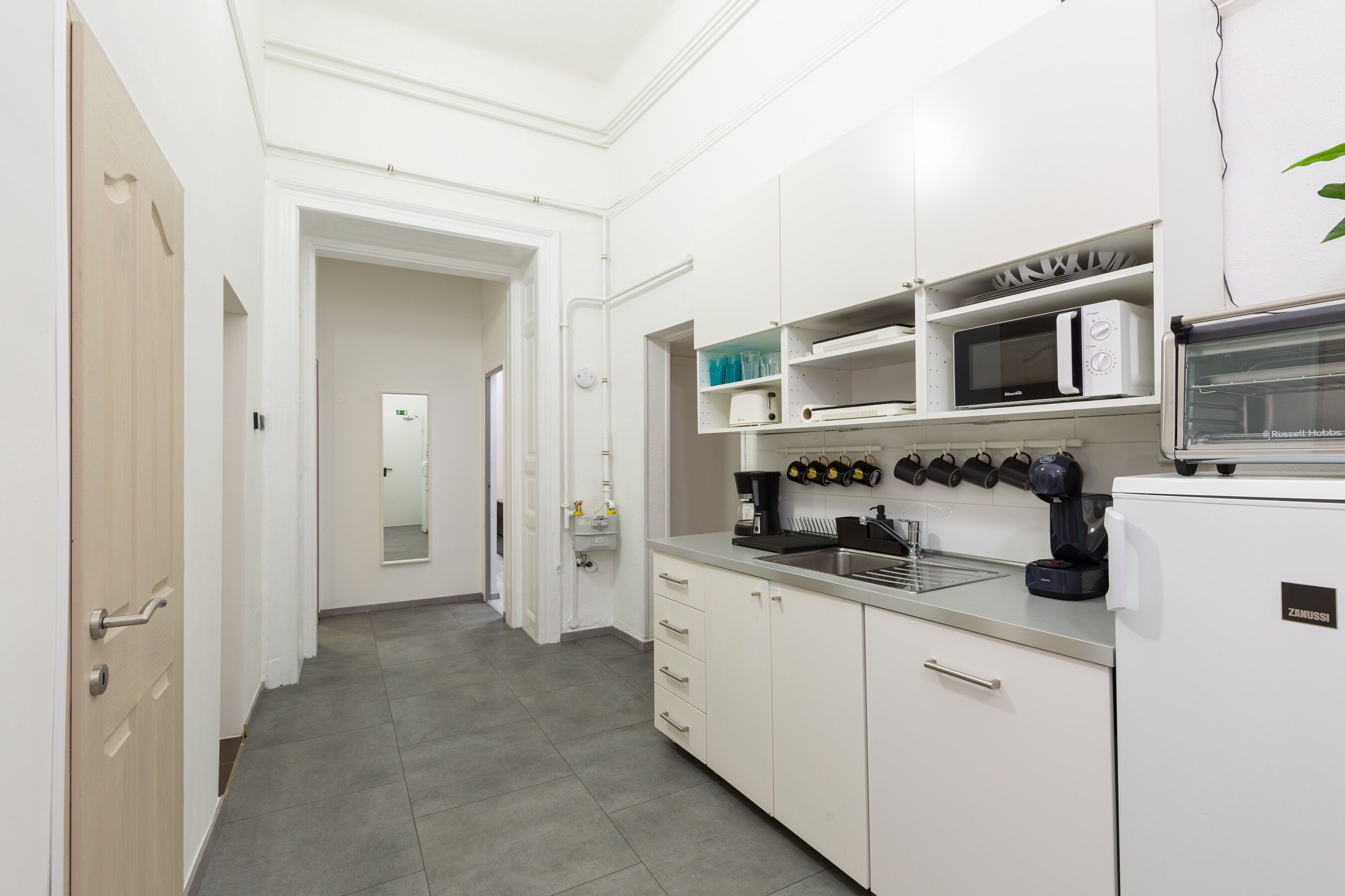 Una cocina moderna con armarios blancos, microondas integrado, cafetera y lavamanos.