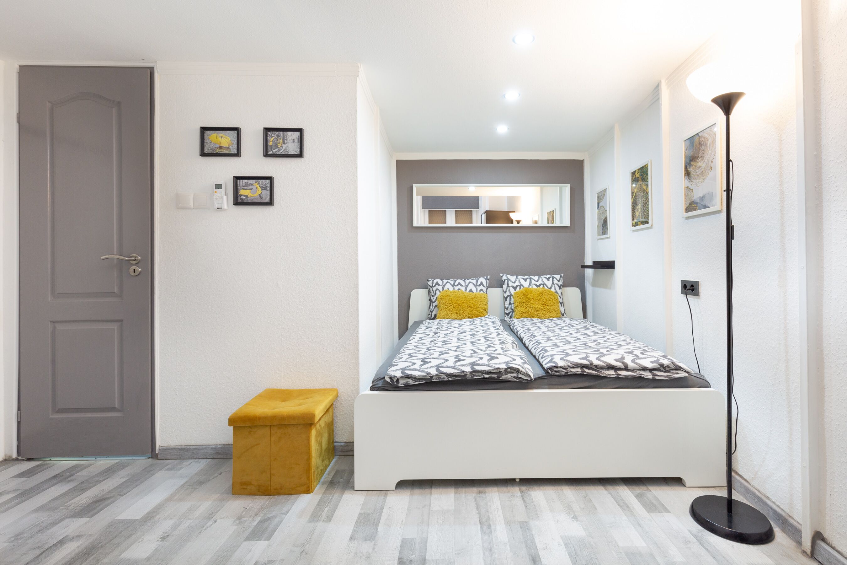Une chambre à coucher avec un lit, un banc, une porte et une lampe sur pied.