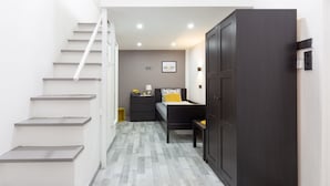 Un couloir avec un escalier, un lit avec une tête de lit, une armoire et un luminaire fixé au mur.