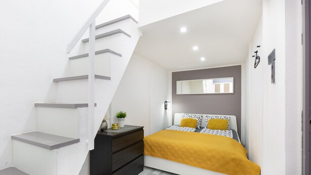 Une chambre à coucher avec un lit, une commode, un miroir et un escalier.