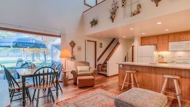 A spacious kitchen with wooden cabinets, a white refrigerator, and a bar area with stools. There is a dining area with a table and chairs, and a large window with a view of the outdoors. - Perfect Location, Near Golf Course, SHARC passes (Sunriver)