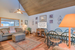 A cozy living room with a sofa, ottoman, and dining table set. There are framed pictures on the wall and a sign that reads "Sunset Lodging in Summer." - Perfect Location, Near Golf Course, SHARC passes (Sunriver)