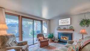 A cozy living room with a fireplace, comfortable seating, and a large sliding glass door leading to an outdoor area. - Perfect Location, Near Golf Course, SHARC passes (Sunriver)